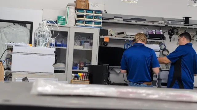 Two AMP Tech technicians working together at a lab bench beside the parts drawers