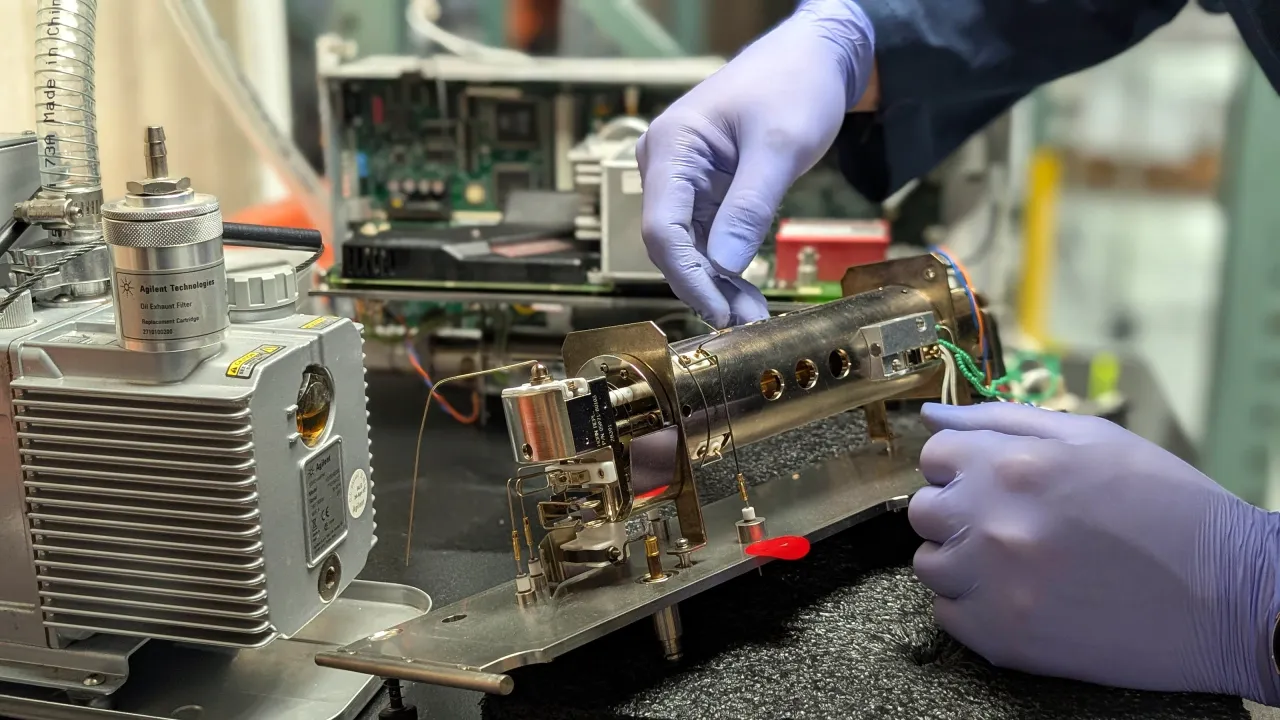 Gloved hands working on a mass spectrometer ion source during a repair at AMP Tech