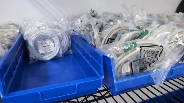 Bins of bagged instrument parts and cables in AMP Tech's parts inventory