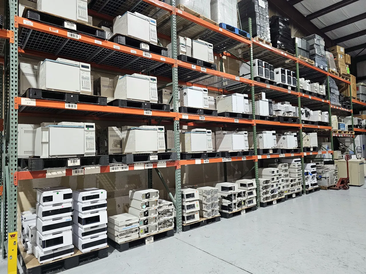 Racks of refurbished gas chromatographs above stacks of HPLC modules on pallets in AMP Tech's warehouse