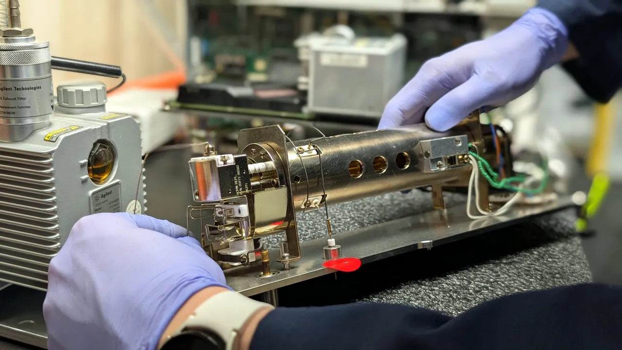 Gloved hands reassembling a mass spectrometer ion source on the bench at AMP Tech